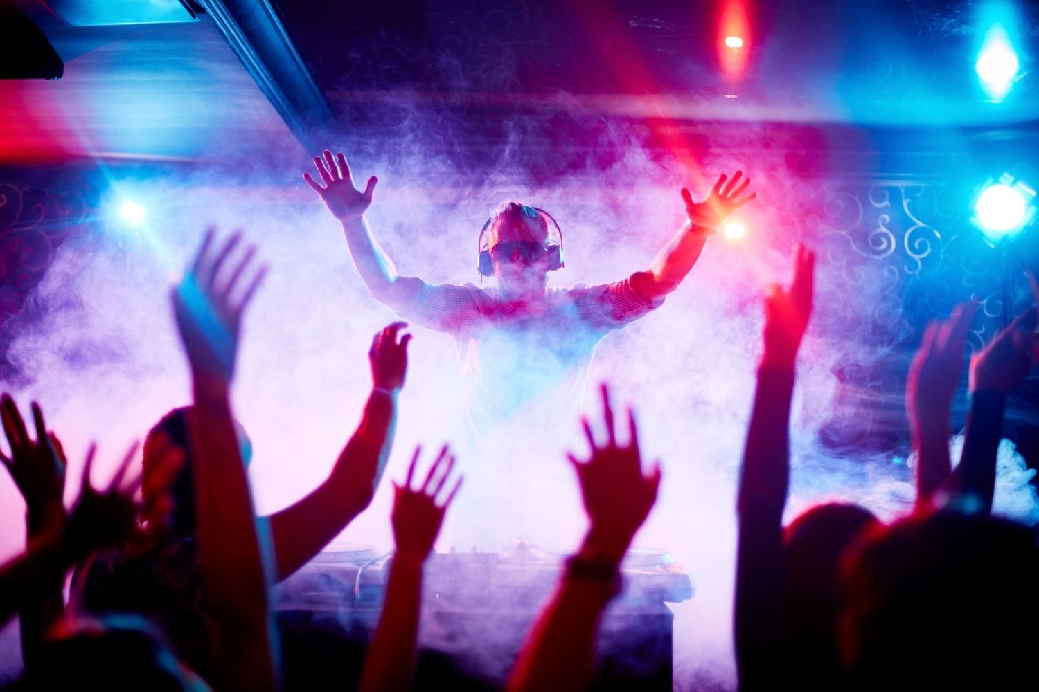 A crowd with arms raised in front of a lit stage