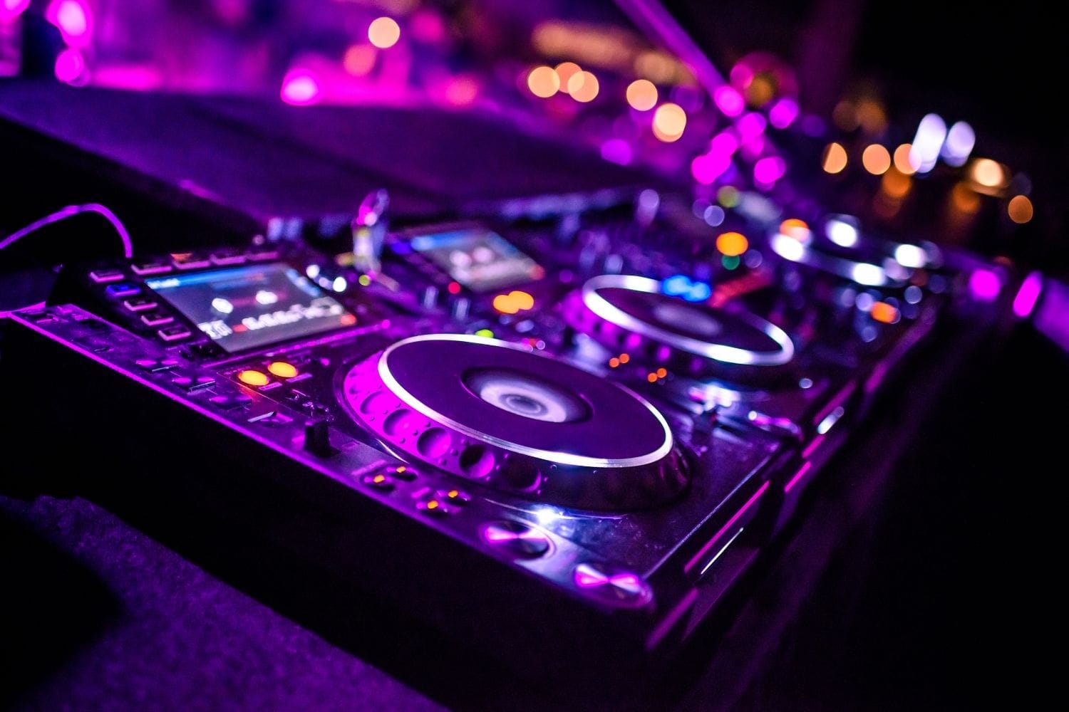 Close-up of illuminated CDJ decks under purple club lighting