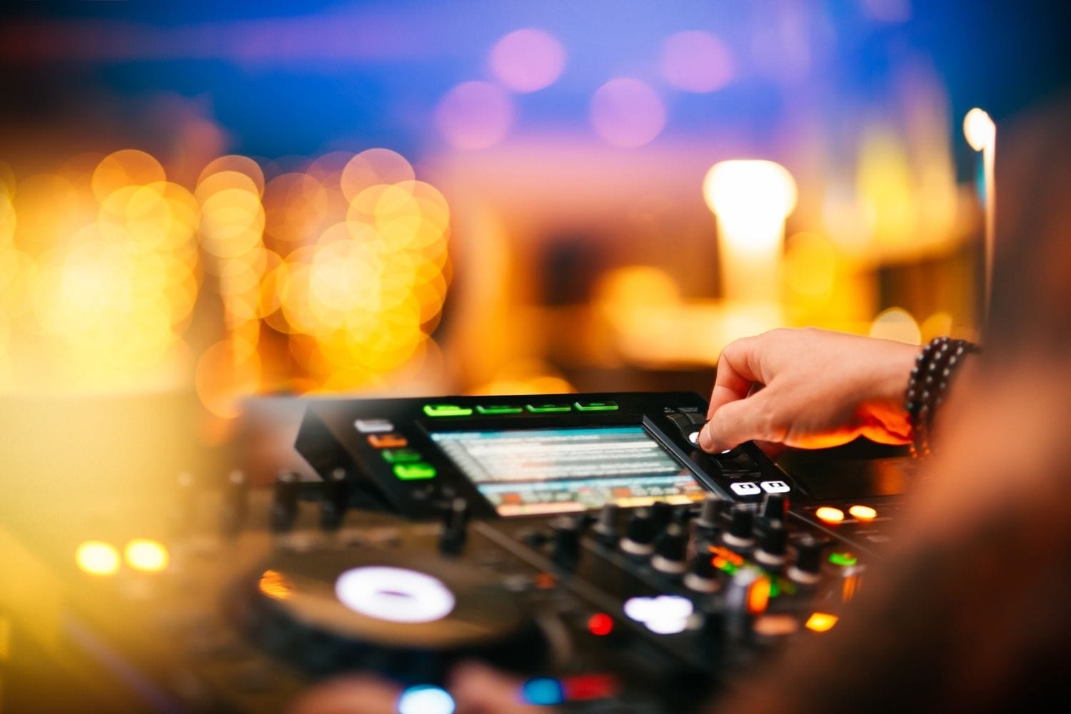 A hand adjusting a DJ controller with warm golden bokeh lights behind