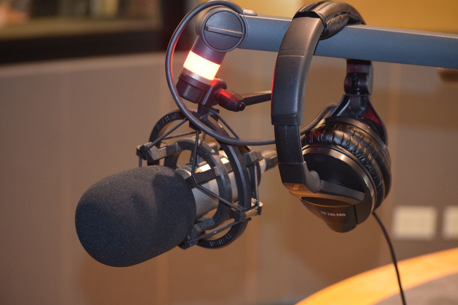 A broadcast microphone and studio headphones on a radio desk with a warm on-air glow