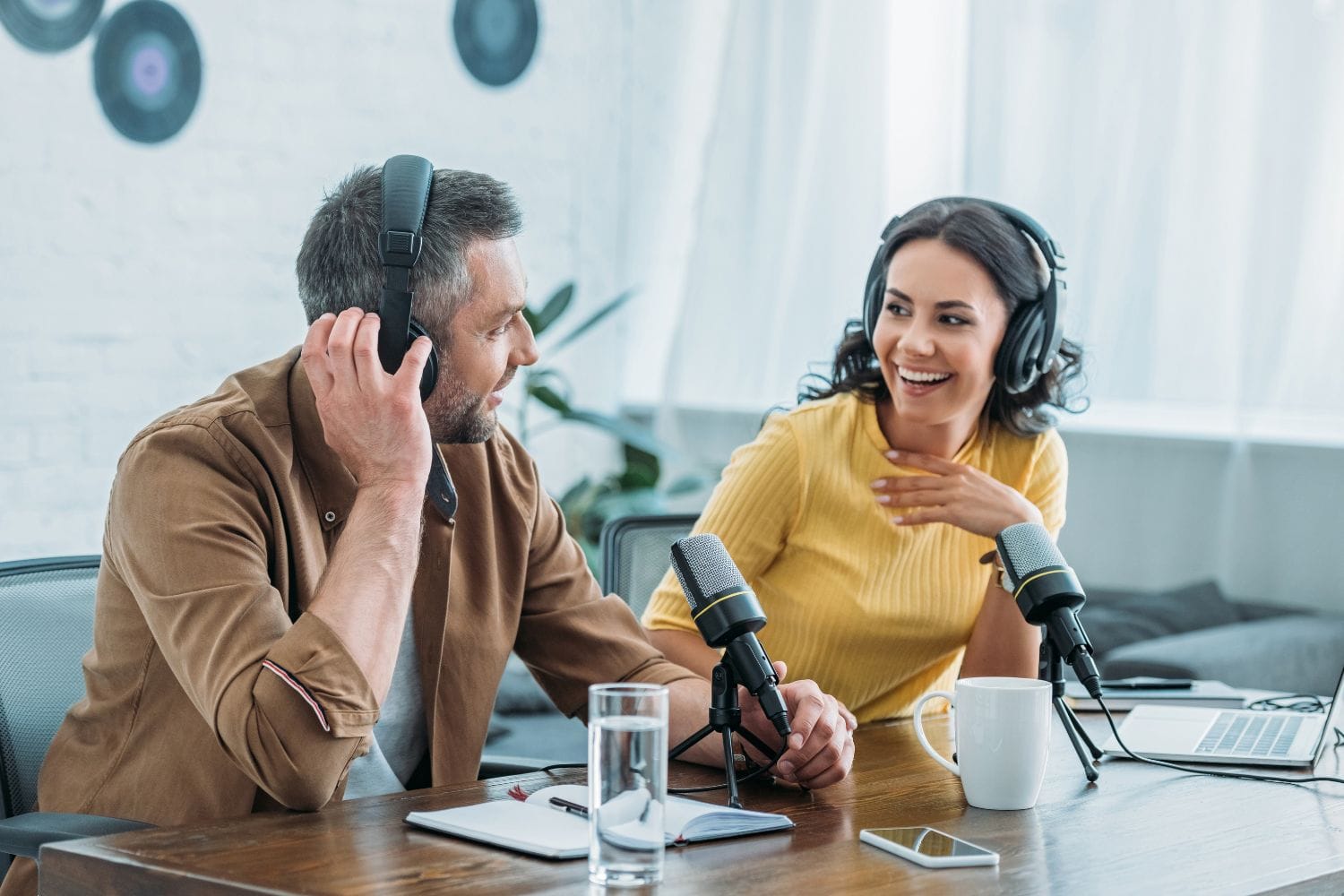 Two radio presenters wearing headphones laughing together at studio microphones