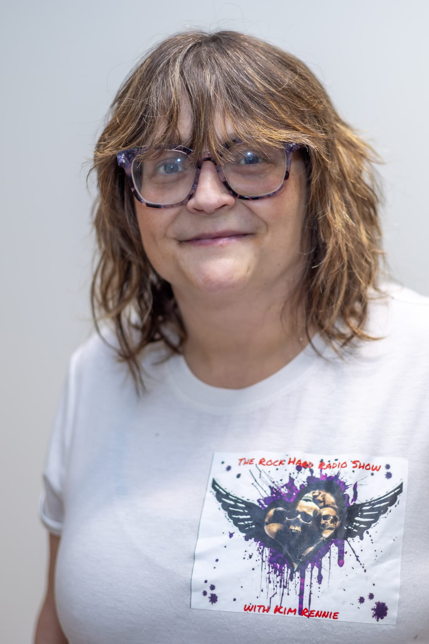 Kim Rennie smiling to camera, wearing a Rock Hard Radio Show t-shirt