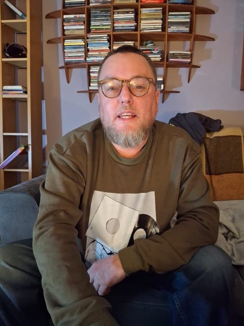 Robert Johnson, founder of Erebus Radio, sitting in front of shelves of CDs and records