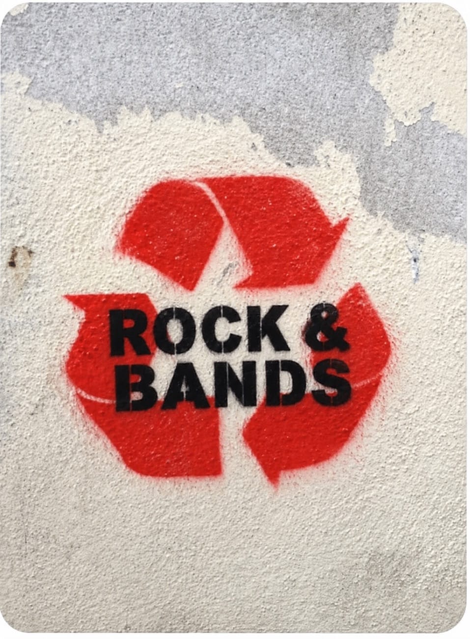 Red spray-painted recycling arrows with stencilled black text reading Rock and Bands on a rough concrete wall